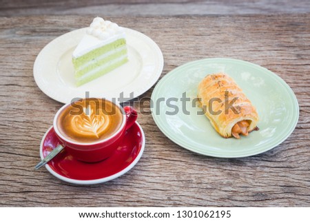 red cup coffee with flower picture milk on top, coconut cream cake and sausage pie, all put on bark wooden table