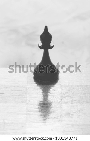 Chess board and black bishop chess piece stand on a light table. Black and white photography