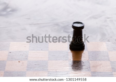 Chess board and  black rook chess piece lying on a light table.