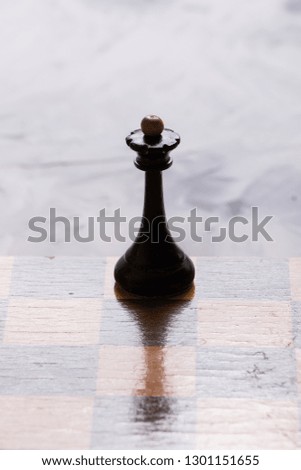 Chess board and black king chess piece lying on a light table.