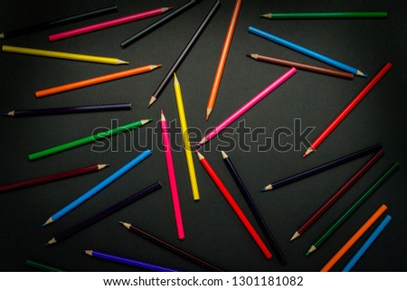 Color pencils scattered throughout the frame on a black background. Flat lay, top view