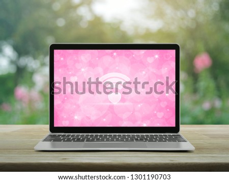 Heart love wifi flat icon on modern laptop computer with love heart screen on wooden table over blur flower and tree in garden, Internet online love connection, Valentines day concept