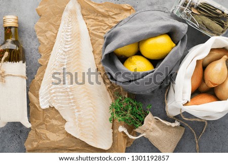 Zero waste food shopping. Sea white fish cod fillet ingredients. Onions, lemons, olive oil, thyme on a light gray background. Top view.