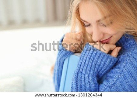 Beautiful young woman sitting with book on bed and dreaming at home. Winter atmosphere