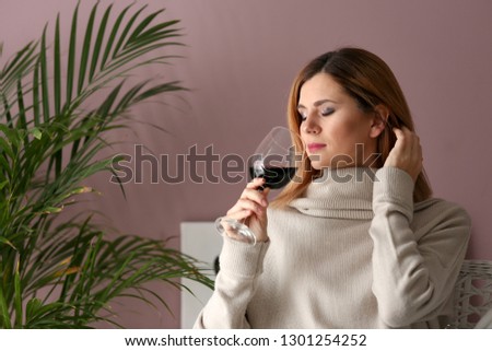 Beautiful woman smelling tasty wine at home