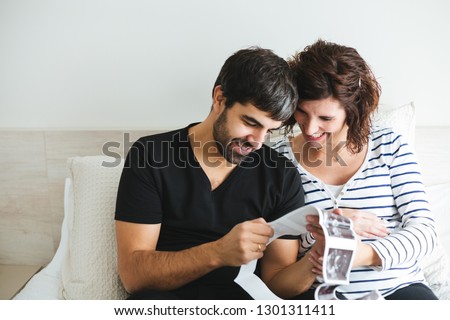 Happy and excited pregnant couple looking at the ultrasound images of their baby sitting on the bed Royalty-Free Stock Photo #1301311411