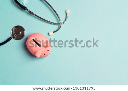 Piggy bank with stethoscope on blue background. Top view with copy space. Concept for financial checkup or saving for medical insurance costs. Royalty-Free Stock Photo #1301311795