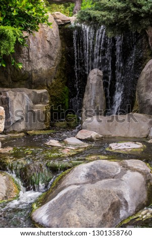 A small waterfall that flows from the green rainforest to a large lake, surrounded by large rocks