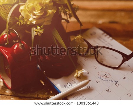 Rose Flower bouquet,red Alarm clock,and eyeglasses,on the calendar,written reminder to Anniversary.Valentines day,February 14,on empty old wood planks.Rustic still life and dark background,dimly light