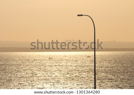 Looking across the sea to a silhouette of land at sunset. Orange sky in the background and a curved light pole. Copy space. View from La Perouse, Sydney
