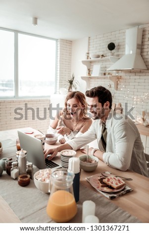 Enjoying the movie. Bearded handsome man and his cute long-haired wife looking amused while watching a movie on a laptop