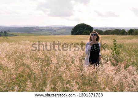 young woman admiring the landscape in an open field with green lawn and flowers at sunset.