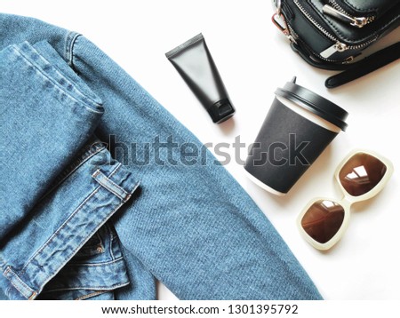 Flat lay photo fashion outfit. Stylish blue denim jacket, jeans, hand cream, paper cup of coffee, sunglasses and small black bag. Top view lifestyle feminine photo for blog