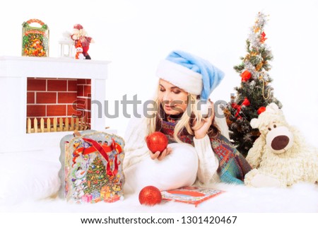 Happy woman in blue hat and white sweater on Christmas Eve near the Christmas tree with a fireplace, candy and toys