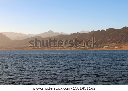 Picturesque landscape of the Red Sea shore, beach with some buildings, sand. High mountains at the background. Summer vacation concept. Red Sea, Dahab, Egypt. 