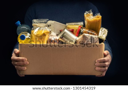 A man holding a donation box of different products on dark background Royalty-Free Stock Photo #1301454319