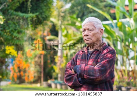 Senior man face is worried, standing arms crossed and looking away to side at the garden. Space for text