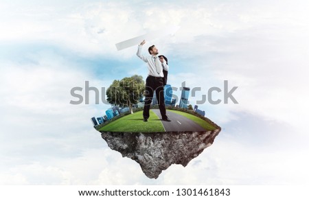 Horizontal shot of confident and young businessman in suit throwing big white arrow in the air while standing on flying island with cloudy skyscape on background.