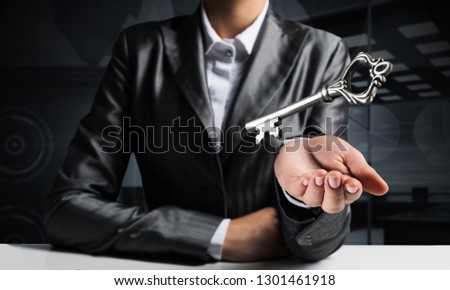 Cropped image of businessman in suit keeping big key in hand with office view on background.