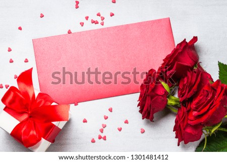 Red roses, greeting card and present box on white stone table. Holiday background.