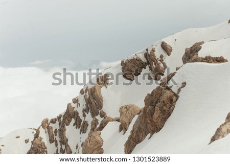 Snow-covered mountain range.Snow-covered mountain peaks. Clouds over rocky rocks. Deserted mountain peaks in the snow. Picturesque mountain landscape.