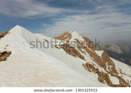 Snow-covered mountains against the blue sky.Snow-covered mountain peaks. Clouds over rocky rocks. Deserted mountain peaks in the snow. Picturesque mountain landscape.