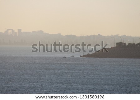 A landscape looking out over the sea to silhouettes of land. A soft orange sky. Seascape view from La Perouse, Sydney Australia