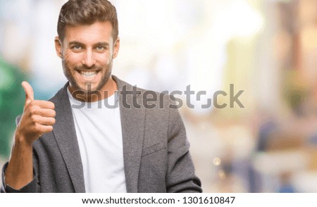 Young handsome business man over isolated background doing happy thumbs up gesture with hand. Approving expression looking at the camera with showing success.