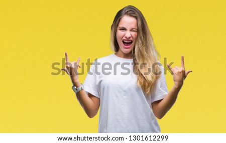 Young beautiful blonde woman wearing casual white t-shirt over isolated background shouting with crazy expression doing rock symbol with hands up. Music star. Heavy concept.