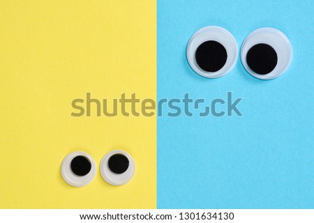 Two pair googly eyes on blue-yellow background look at each other, mad funny toys eyes close-up.
