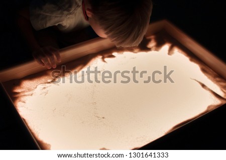the boy plays on the light table with sand