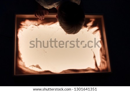 the boy plays on the light table with sand