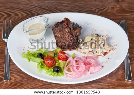 beef medallions with mushrooms, lettuce, olives, cherry tomatoes and onions. served with white sauce, on a wooden table in the restaurant