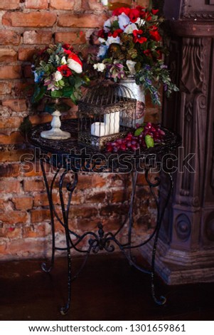 Gothic interior details. Dark room with a brick wall, metal table with cage with candles, fruits and vases with flowers