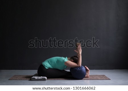woman practicing yoga, Seated forward bend pose, using block and bolster Royalty-Free Stock Photo #1301666062