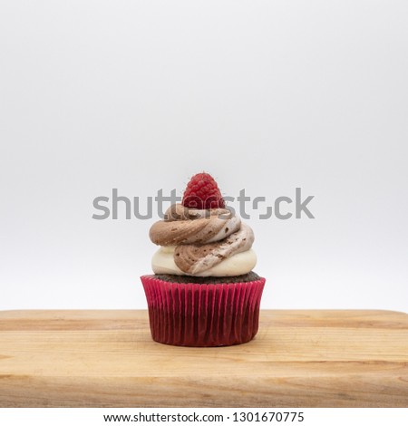 Chocolate cupcake topped with chocolate vanilla swirl frosting adorned with raspberry on white background