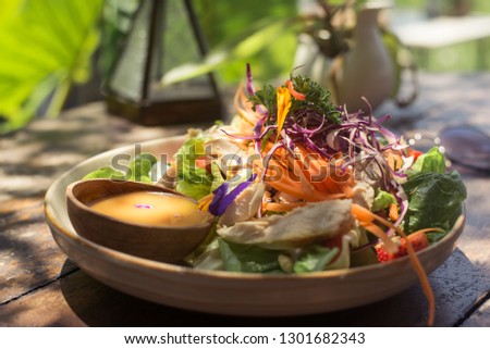 Bowls vegetable salad on an old wooden table, carrots, lettuce, strawberries, chicken honey dressing, typical food in a cafe in Bali, Indonesia