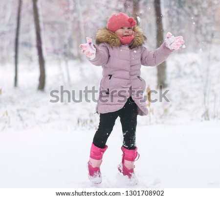 sweet, smiling little girl spending a nice time outdoor,enjoy in the snow flakes and winter games. One small girl 2-3 years,catch the snowflakes,throw it the snow in the air.