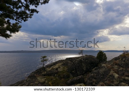 Sun rays break through clouds on the background of the stone Bank of the river, Ladoga in Karelia