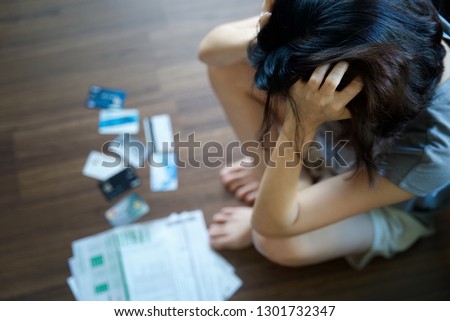 Stressed young Asian woman holding her head feeling headache and thinking how to find money to pay credit card debt and all bills that put in front of her. Financial problem concept. Royalty-Free Stock Photo #1301732347