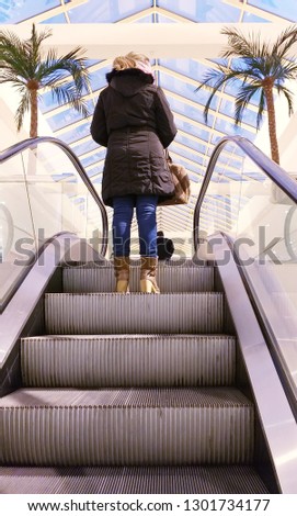 WOMAN ON A MECHANIC GREY ESCALATOR MADE OF STEEL TO GO UP STAIRS OR TO GO DOWN STAIRS TO OTHER FLOOR IN THE INTERIOR OF A SHOPPING MALL WITH NOBODY. VERTICAL PHOTO