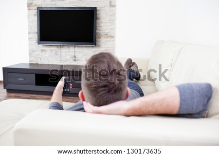 Single man on the couch watching tv, changing channels Royalty-Free Stock Photo #130173635