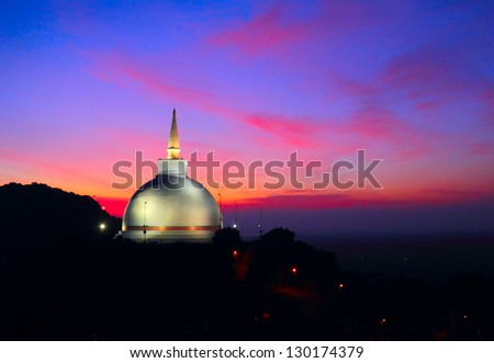 Beautiful white Maha Seya Stupa and black rock against the background of colorful sunset with dramatic pink and blue cloudy sky, Mihintale - mountain peak near Anuradhapura, Sri Lanka island