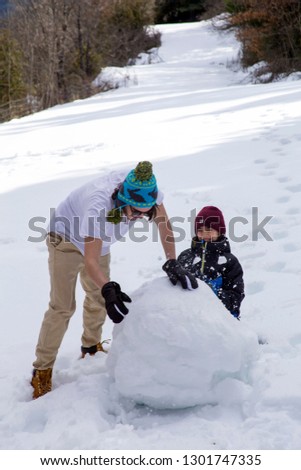 Brothers make a snowman in a winter forest in the mountains.