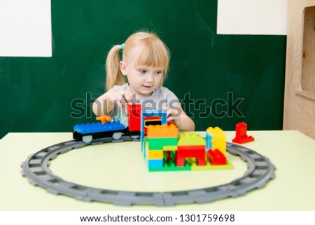 Five year old blond girl playing with a train on a chalkboard background. Play centre . Happy kid
