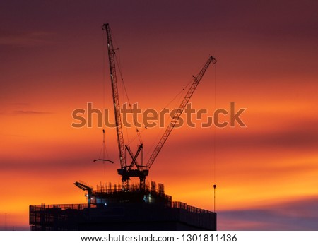 Photo of crane construct on the roof top of skyline building on colorful twilight sunset sky background . Crane on orange sky in big city. Dust and air pollution made light scattering.