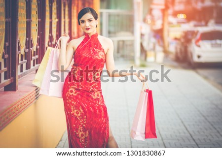 Chinese girl wearing Cheongsam and smile happily. Holding her shopping bags after a lot of shopping malls in Chinatown and was walking on the sidewalk. Amid the atmosphere of the evening sun.