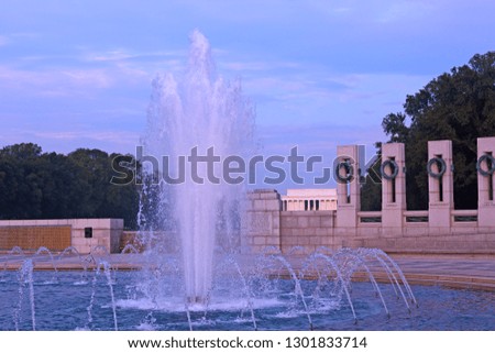Fountain of World War II Memorial and brightly lit Lincoln Memorial on horizon at sunrise, Washington DC, USA. Sunrise on National Mall in US capital.
