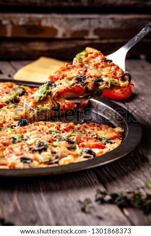 Concept of Italian cuisine, Homemade Italian pizza with salami sausage, tomatoes, with black olives and cheese on a wooden background. copy space