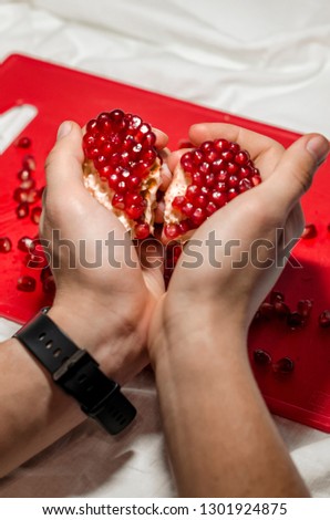 Human hands making a heart of fresh pomegranate pices on the red cutting board. The background is red. Ripe organic food close up. Stay healthy concept. Broken symbol of love.